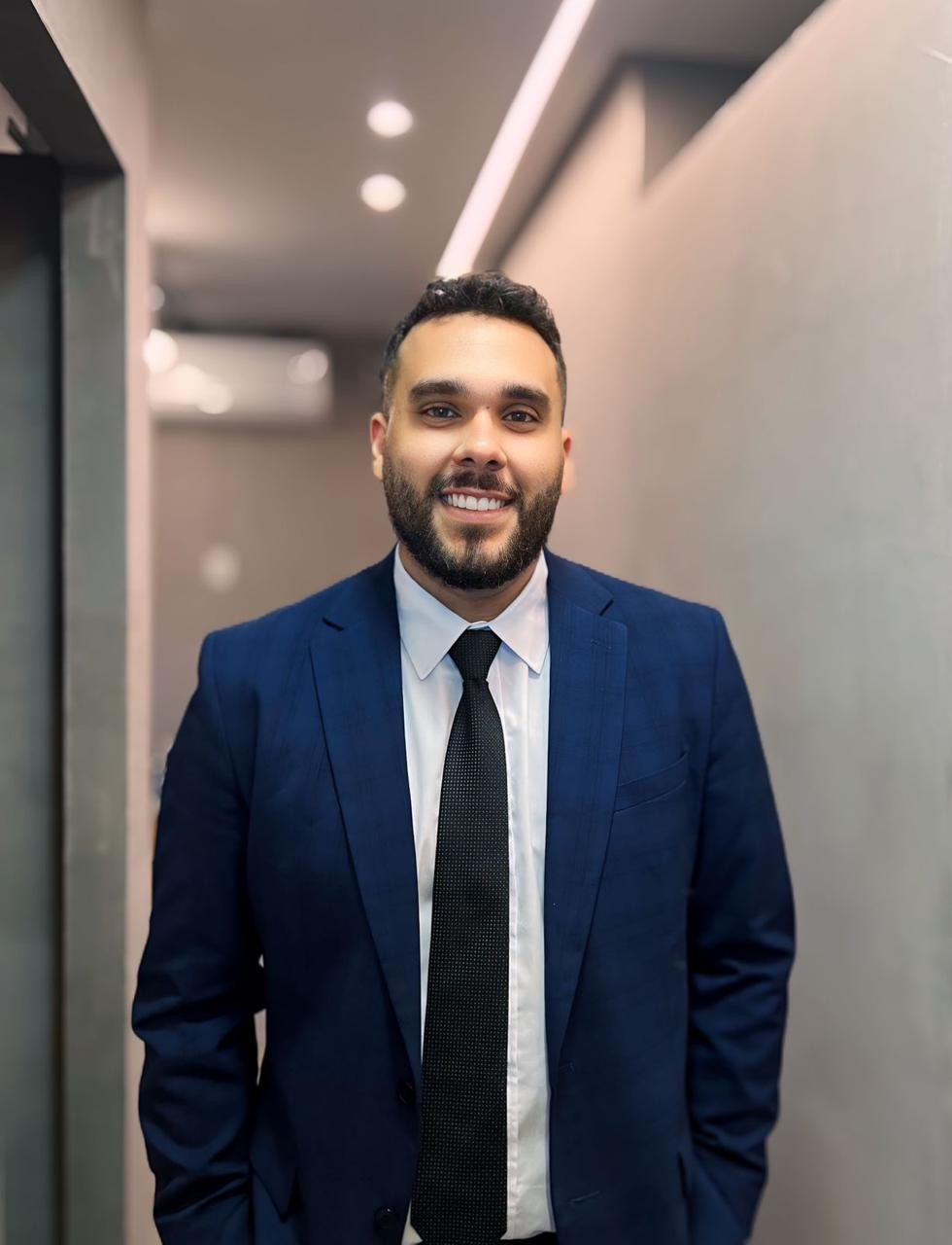 Carlos Henrique Santana Lima, advogado, sorrindo de terno azul no corredor do escritório